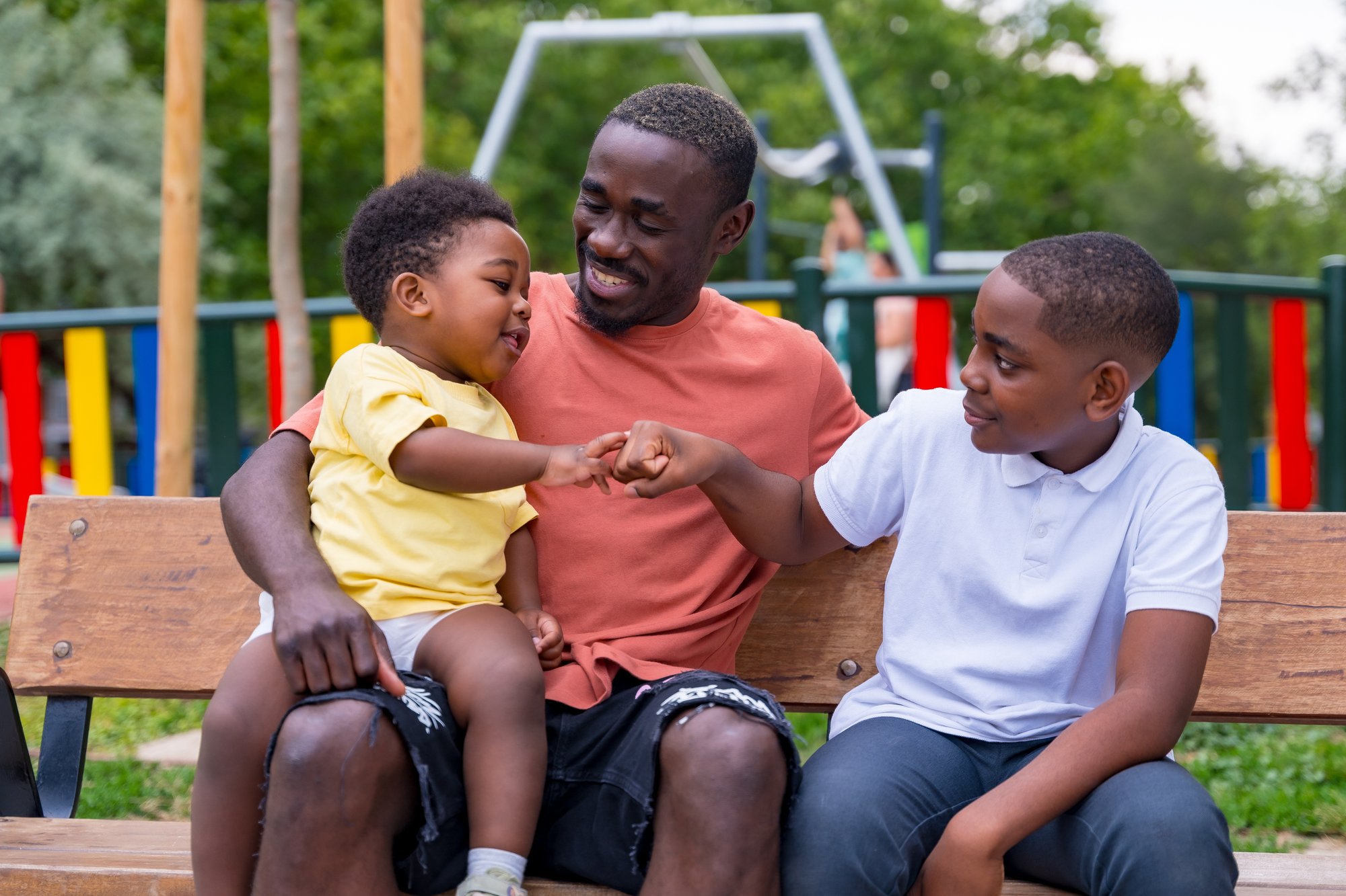 Father and sons on a park bench. The two boys are giving each other a fist bump. 